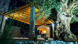 An outdoor patio with a stone wall, a pergola with yellow lighting, and a fireplace. - Villa Vida (Zmijavci)