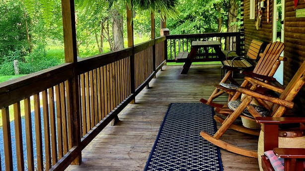 A wooden porch with a railing, a bench, and two rocking chairs.