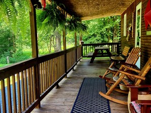 Eine Holzveranda mit Geländer, einer Bank und zwei Schaukelstühlen.