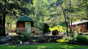 A cabin with a porch, surrounded by lush greenery and a gravel path.