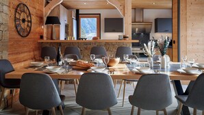 Un espace repas avec une longue table en bois, dressée pour six personnes, entourée de murs en pierre et de poutres en bois.