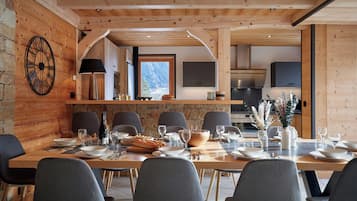 A dining area with a long wooden table set for six, surrounded by stone walls and wooden beams.