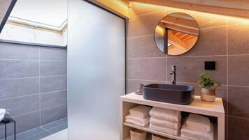 A modern bathroom with a skylight, a round mirror, a vessel sink, and neatly folded towels on shelves.
