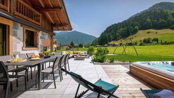 Een houten terras met tuinmeubilair, een jacuzzi en uitzicht op een groene vallei en bergen.