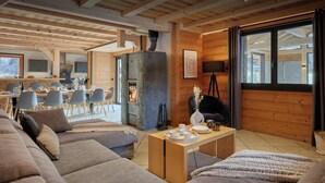 Un salon moderne avec une cheminée en pierre, des murs en bois et un coin repas agrémenté d’une grande fenêtre.