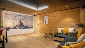 Un salon chaleureux avec un plafond en bois, un canapé agrémenté de coussins, un tableau accroché au mur et un mur orné d’une grande affiche.