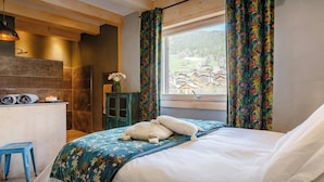 Un dormitorio con cama, una ventana con cortinas, un escritorio de madera y vista a un pueblo.