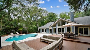 Un espace aménagé au bord de la piscine, avec une terrasse en bois, un canapé intégré et une table avec des chaises.