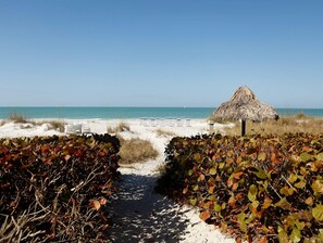 Ein Strandweg führt zu einer mit Stroh gedeckten Hütte, umgeben von Sand und Meer.