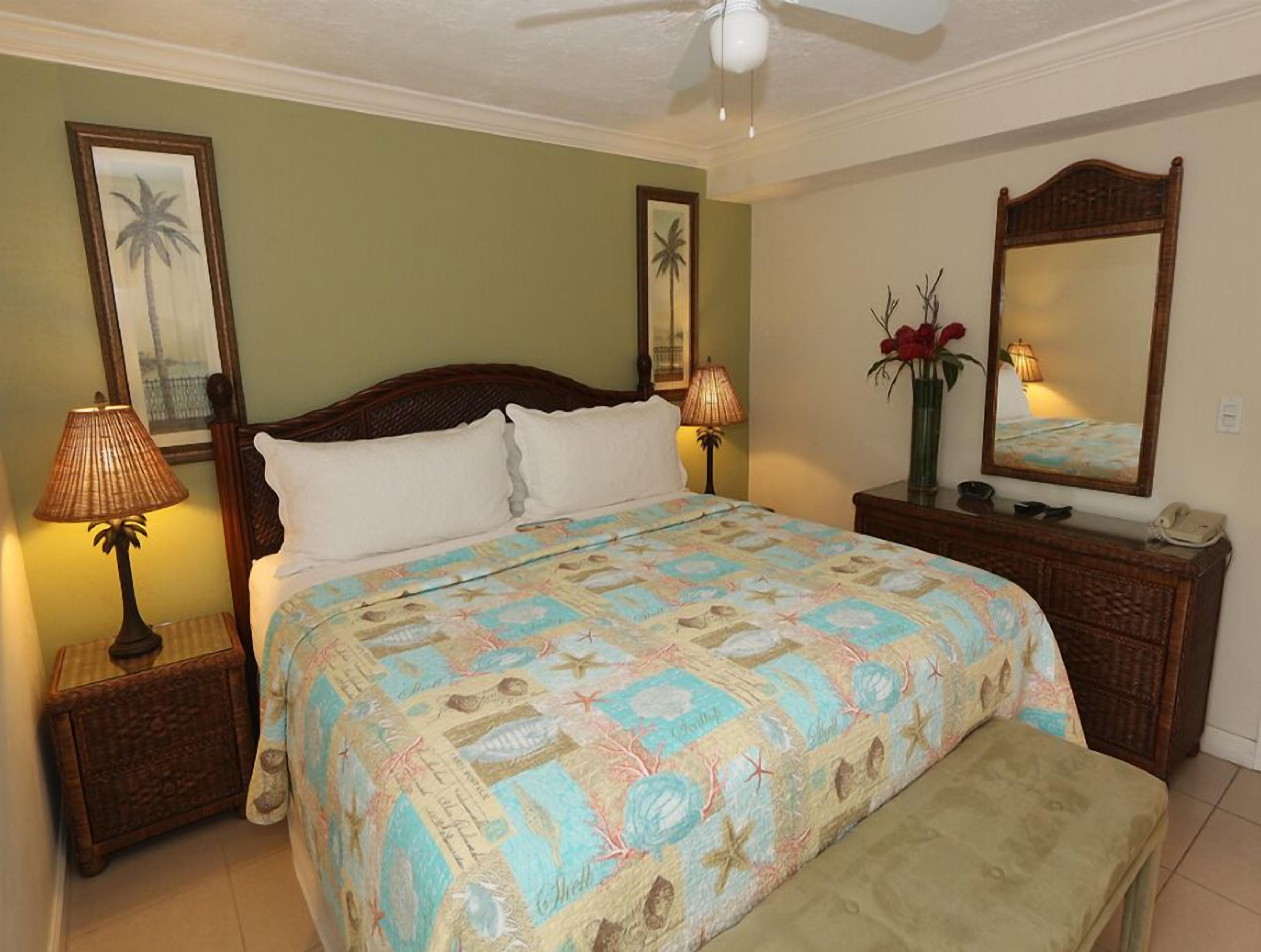 A bedroom with a bed, two bedside tables, a nightstand, a bench, a ceiling fan, a mirror, and wall art.