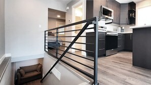 A modern kitchen with dark cabinets, stainless steel appliances, and a black metal staircase railing. - Beautifully Designed Space. One Mile to Mayo Clinic. (Rochester)