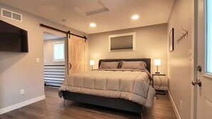 A bedroom with a bed, bedside lamps, a TV mounted on the wall, and a window with blinds. - Beautifully Designed Space. One Mile to Mayo Clinic. (Rochester)