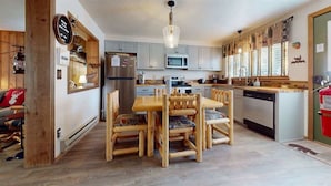 A modern kitchen with wooden furniture, stainless steel appliances, and a dining area with a wooden table and chairs. - Hook and Antler (West Yellowstone)