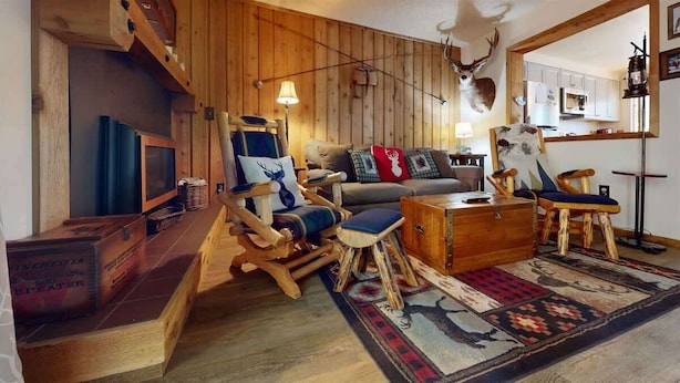 A rustic living room with wooden furniture, a sofa, a coffee table, and a mounted deer head. - Hook and Antler (West Yellowstone)