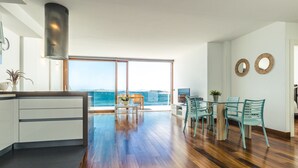 Uma cozinha moderna com uma ilha grande, uma área de jantar com cadeiras azul-turquesa e vista para o mar através de grandes janelas.