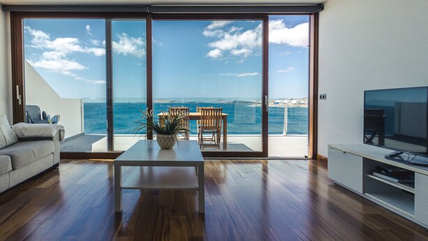 Sala de estar moderna com uma grande porta de vidro deslizante que dá para uma varanda com vista para o mar.