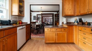 A kitchen with wooden cabinets, a dishwasher, and a dining area with a table and chairs. - Beautiful Craftsman with Off-street parking, EV charger, Yard + Dogs OK! (Seattle)