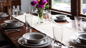 A dining table set with plates, glasses, and cutlery, a vase with flowers, and a window view. - Beautiful Craftsman with Off-street parking, EV charger, Yard + Dogs OK! (Seattle)