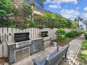 An outdoor kitchen with two grills, a stone backsplash, and a metal cabinet.