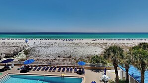 Une vue sur la plage avec une piscine, des chaises longues et des parasols.