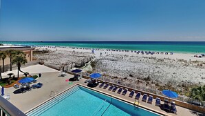 Un espace piscine avec des chaises longues et des parasols, une plage avec des parasols et des transats, et une vue dégagée sur l’océan.