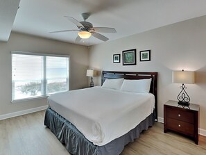 A bedroom with a bed, ceiling fan, bedside lamps, a nightstand, and a window with blinds.