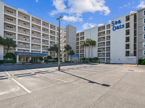 A multi-story hotel with a parking lot in front, featuring a sign that reads 'Sea Oats.'