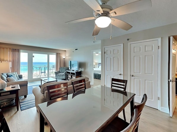 A spacious living area with a large dining table, a ceiling fan, and a view of the ocean.