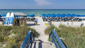 A beach with blue umbrellas and lounge chairs, a wooden structure, and a sign prohibiting tents.