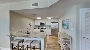 A modern kitchen with white cabinets, stainless steel appliances, and a marble island with bar stools.