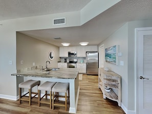 A modern kitchen with white cabinets, stainless steel appliances, and a marble island with bar stools.