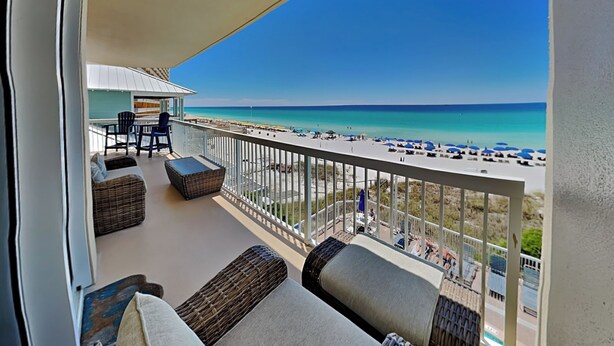 A balcony with a view of a beach, outdoor furniture, and a clear sky.