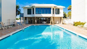 A swimming pool with a poolside area, lounge chairs, and a two-story building with large windows. - Shipwatch Surf & Yacht #201B | Unobstructed Gulf Views! (Perdido Key)
