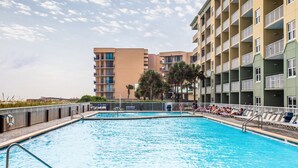 Une piscine avec des chaises longues et, au fond, un bâtiment doté de nombreux balcons.
