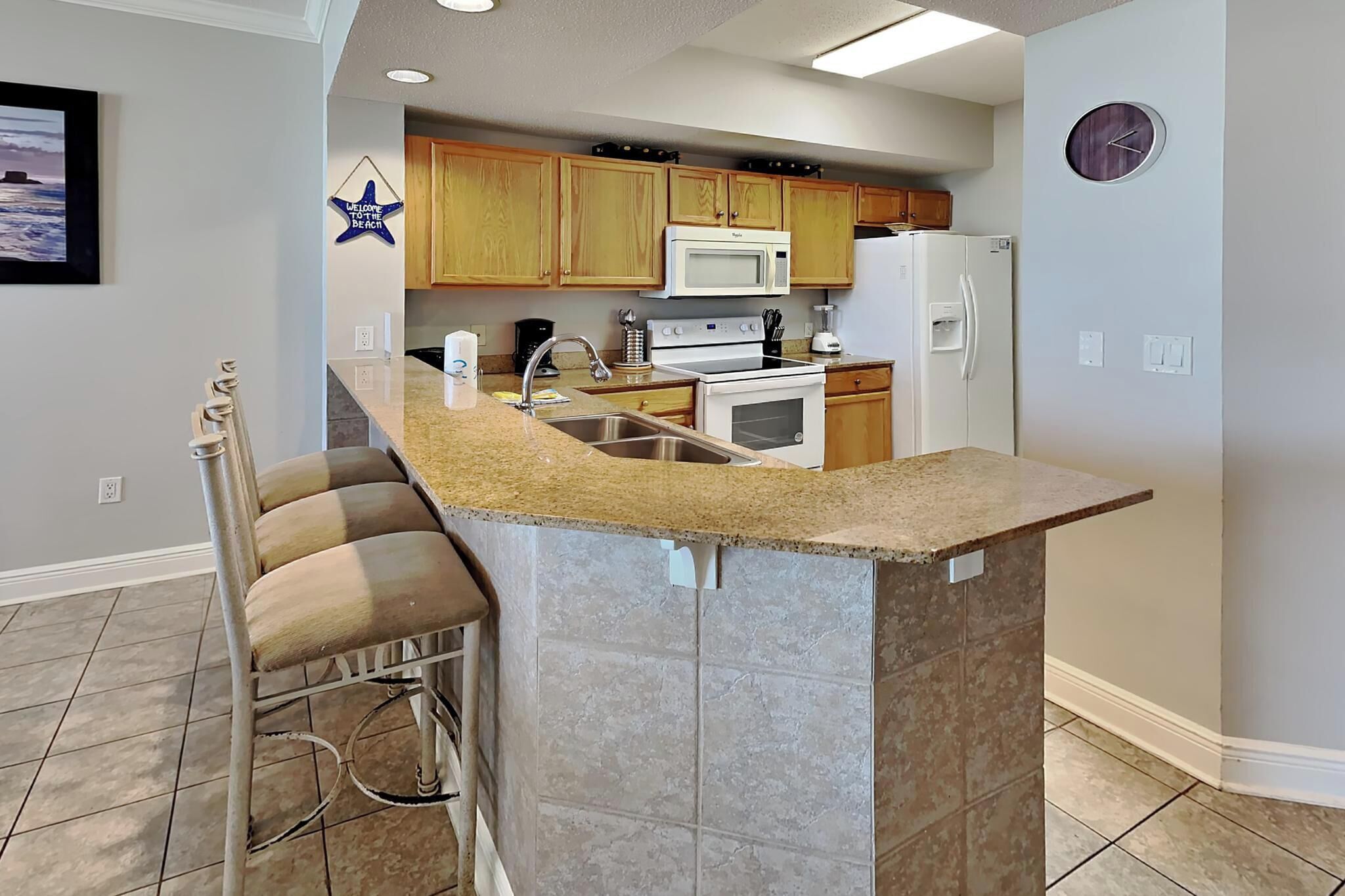 A kitchen with wooden cabinets, a built-in island with a sink, a microwave, a stove, and a refrigerator.