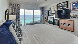 Une chambre avec un grand lit, un ventilateur de plafond, une télévision et une vue sur l’océan.