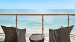 Un balcon avec des fauteuils en osier et une petite table, d’où l’on peut admirer une plage et la mer.