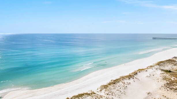 Une plage aux eaux turquoise et limpides, un rivage sablonneux et une jetée qui s’avance dans la mer.