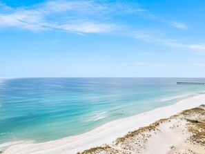 Een strand met helder turquoise water, een zandstrand en een pier die in zee uitloopt.