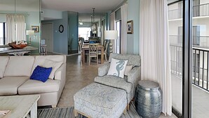 En rummelig stue med sofa, skammel og et spiseområde med stole og bord.
