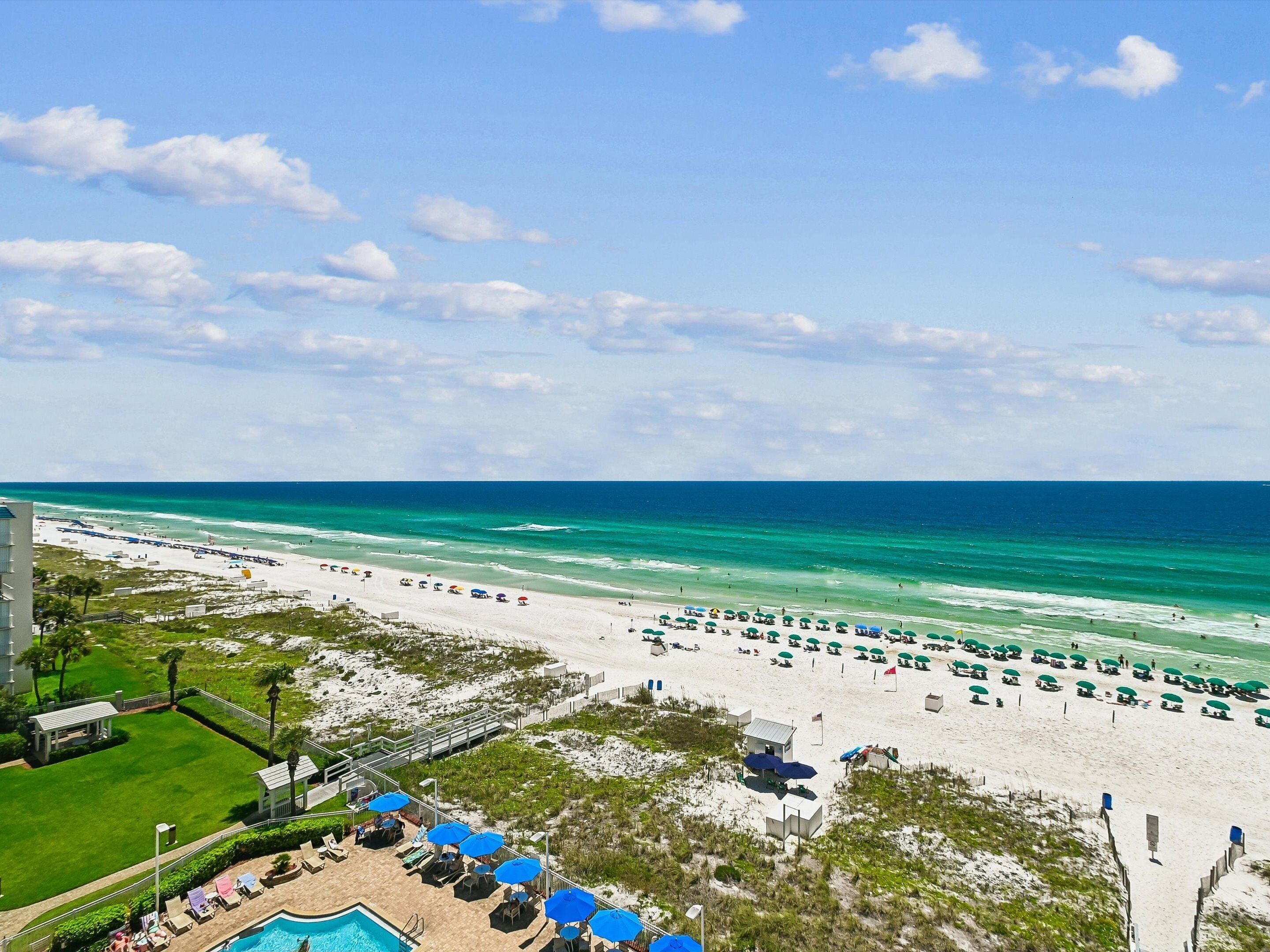 A beach resort with a swimming pool, beach umbrellas, and a view of the ocean.