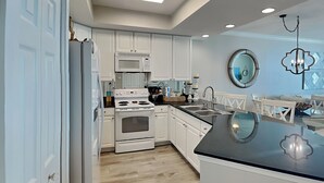 A modern kitchen with white cabinets, a stainless steel sink, and a large island. - Gulf Front Condo with Stunning View and Resort Amenities (Gulf Shores)