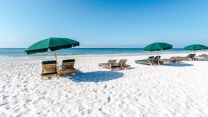 A beach with white sand and clear blue water. There are several wooden lounge chairs and green umbrellas. - Gulf Front Condo with Stunning View and Resort Amenities (Gulf Shores)