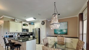 A modern kitchen with white cabinets, a central island with seating, a stainless steel refrigerator, and a hanging chandelier. - Beach Condo, Lake Views! (Orange Beach)