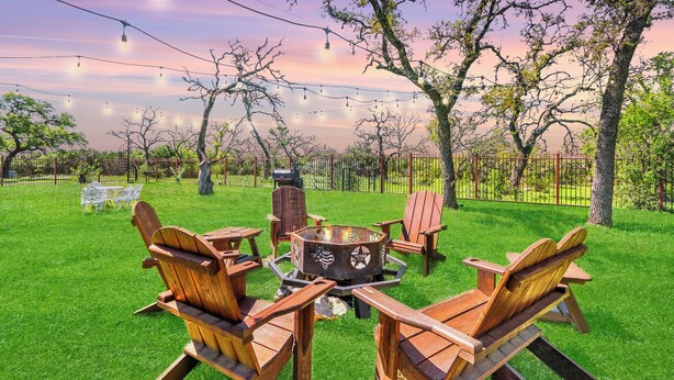A backyard with a fire pit, wooden chairs, and string lights. - 60-Acre Retreat w/ Hot Tub, Firepit & Pet-Friendly! (Wimberley)