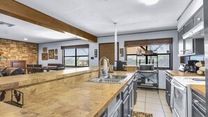 A modern kitchen with a wooden island, stainless steel appliances, and a stone accent wall. - 60-Acre Retreat w/ Hot Tub, Firepit & Pet-Friendly! (Wimberley)