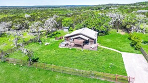 A single-story building with a sloped roof, surrounded by a fenced garden with trees and a clear sky. - 60-Acre Retreat w/ Hot Tub, Firepit & Pet-Friendly! (Wimberley)