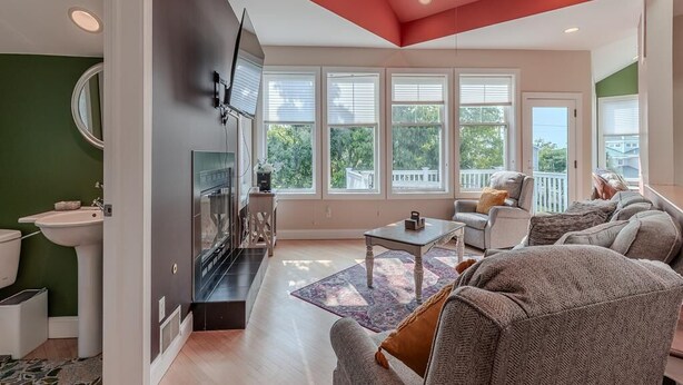 Un salon spacieux doté d’une grande fenêtre, d’un ventilateur de plafond et d’un coin cuisine visible à travers une porte ouverte.
