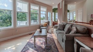 Un salon spacieux doté de grandes fenêtres, d’un ventilateur de plafond et d’un coin salon confortable.