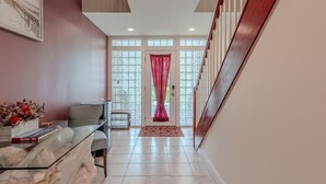 Un couloir avec une table en verre, une chaise et une porte surmontée d’un rideau rouge.